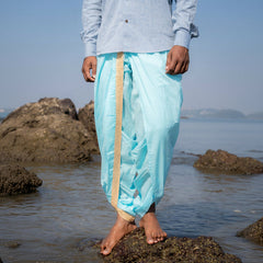 Person wearing light blue dhoti and shirt standing on a rocky beach.