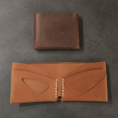 Two brown leather wallets on a light wooden surface