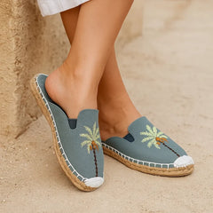 Blue espadrilles with palm tree design worn on a sandy surface