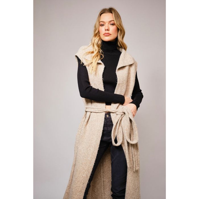 long beige knit vest with waist tie over a black turtleneck and pants, styled in modern western fashion