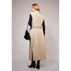 back view of long beige knit vest with waist tie over a black turtleneck and pants, styled in modern western fashion