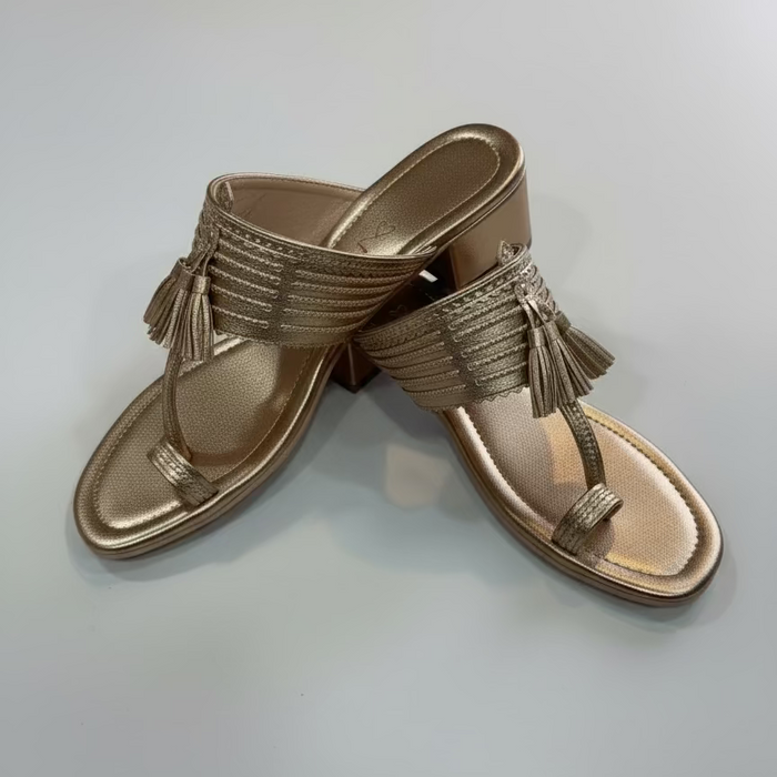 Pair of gold sandals with tassels on a light gray background