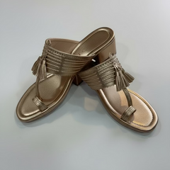 Pair of gold sandals with tassels on a light gray background
