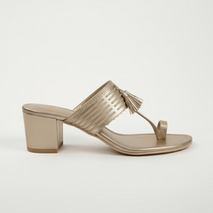 Gold sandals with fringe details worn by a person on a white background
